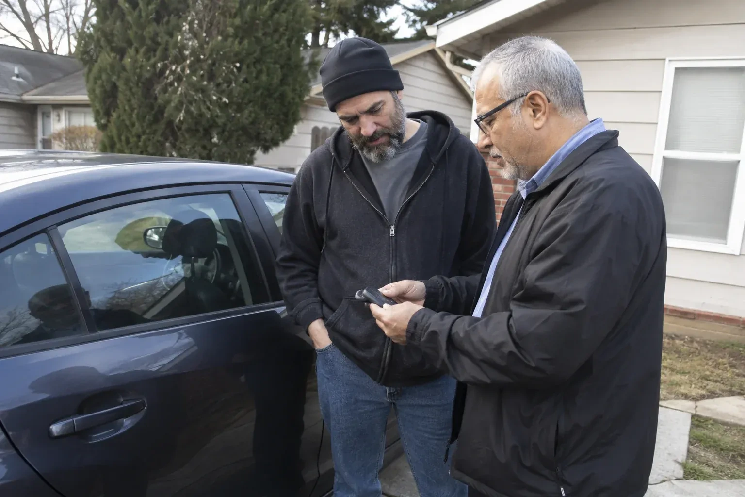 Two adults discussing a key fob beside a parked car. — Car Lockout Service, Georgina
