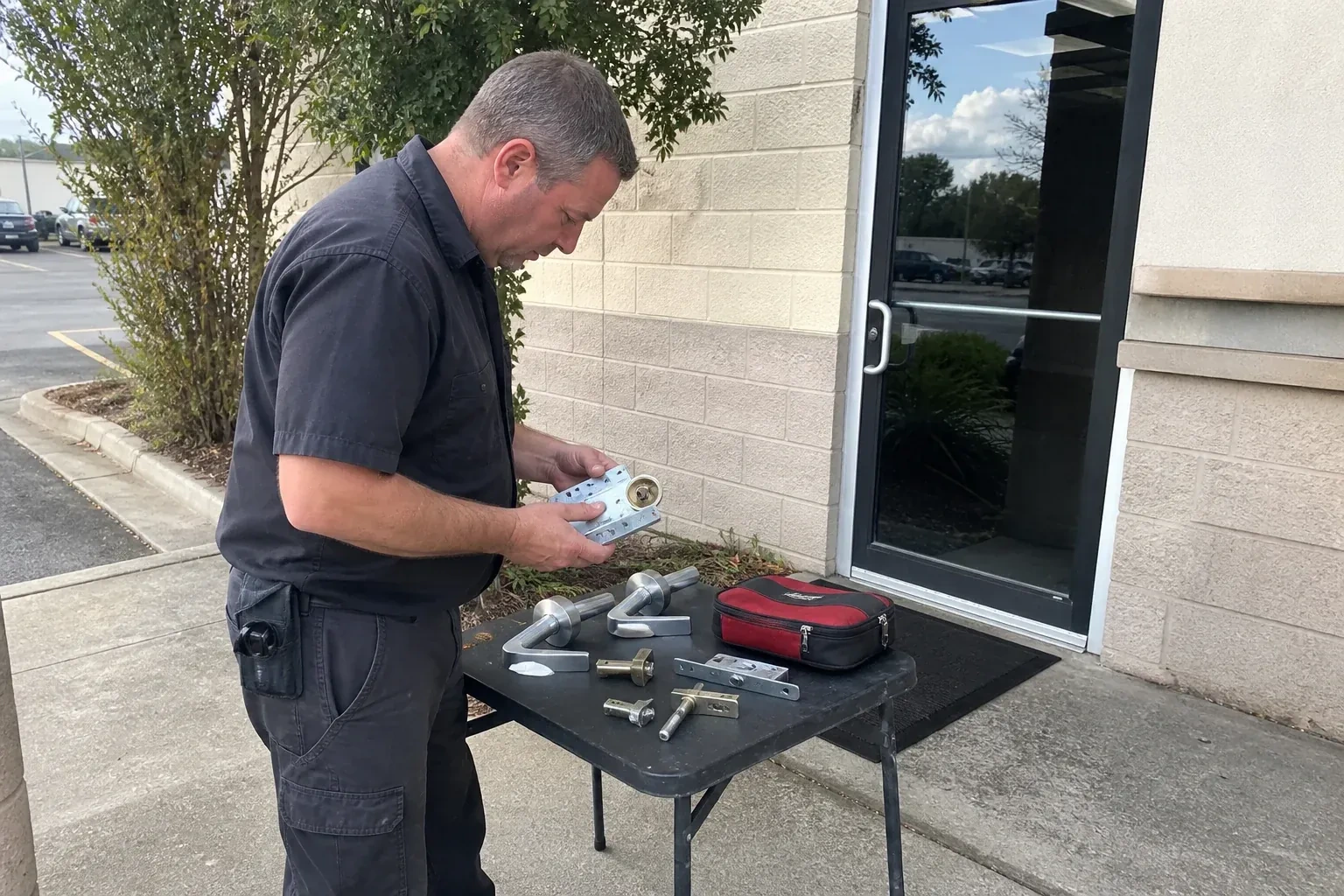 Technician examining detached commercial lock hardware on a table outside a shop entrance. — Business Lockout Service, Georgina