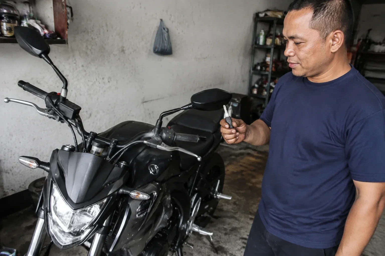 Person holding a key beside a black motorcycle in a garage. — Motorcycle & Scooter Keys, Georgina
