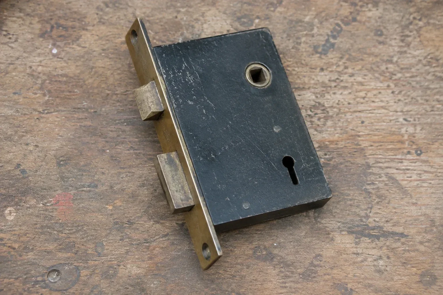Closed mortise lock case with spindle opening, keyhole, latch and deadbolt on a wooden workbench. — Vintage Mortise Lock Service, Georgina